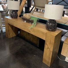 a wooden table with two lamps on it and some chairs in the backround