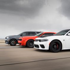 three different colored cars driving down the road in front of dark storm clouds on a cloudy day