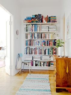 a living room filled with lots of books on top of a white book shelf next to a wooden dresser