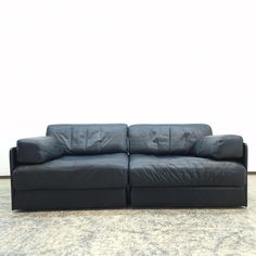 a black leather couch sitting on top of a carpeted floor next to a white wall