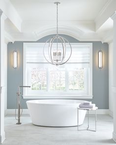 a large white bathtub sitting under a window next to a chandelier in a bathroom