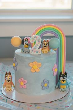 a birthday cake is decorated with cartoon characters and rainbows on the table next to a window