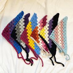 five crocheted hats are lined up on a white sheet and one has a knot at the end