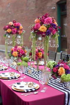 the table is set with black and white striped linens, pink flowers, and tall vases