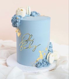 a blue and gold baby shower cake on a white table cloth with flowers around it