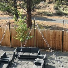 an outdoor seating area is set up with lights strung across the fence and trees in the background