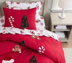 a bed with red comforters and christmas decorations on the sheets, along with a teddy bear