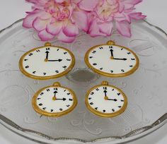 three small clocks sitting on top of a glass plate next to pink flowers and petals