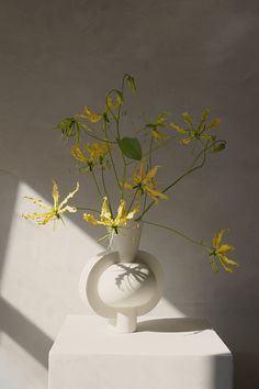 a vase with yellow flowers in it sitting on a white pedestal next to a wall