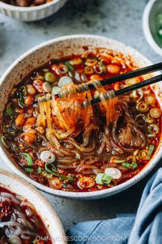 chopsticks are being used to stir noodles in a bowl with red sauce and green onions