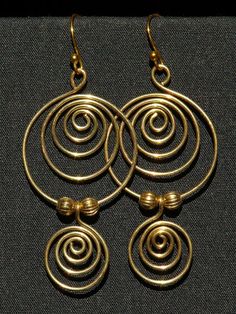 three gold spirals are hanging from the ends of two hoop earrings on a black background