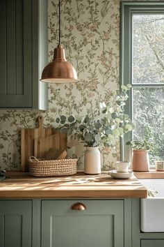 a kitchen with green cabinetry and wallpaper has a copper light hanging over the sink