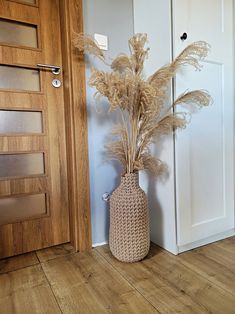 a vase filled with dry grass sitting on top of a wooden floor next to a door