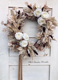 a wreath with white roses and feathers hanging on a door frame in front of a sign