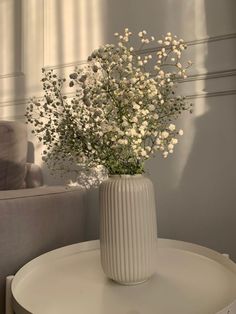 a vase filled with white flowers sitting on top of a table next to a couch