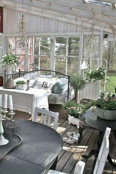 an outdoor room with white furniture and plants on the table, in front of a screened porch