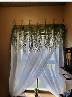 an open window with white curtains and plants hanging from it's rodulage