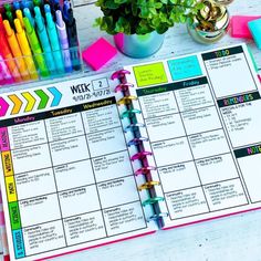 an open planner with markers and pens next to a potted plant on a table