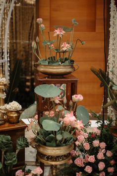 three tiered vases filled with pink flowers on top of a wooden table covered in greenery