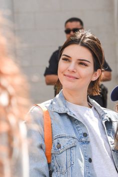 a young woman is smiling and wearing a jean jacket while standing in front of a group of people