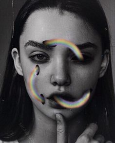 a woman with rainbow painted on her face and fingers in front of her face, looking at the camera