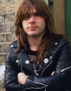 a man with long hair wearing a leather jacket and standing in front of a building