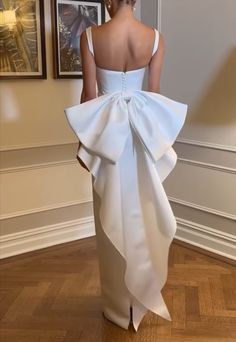 the back of a woman in a white dress with a large bow on it's tail