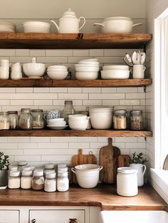 shelves filled with white dishes and bowls on top of wooden counter tops in a kitchen