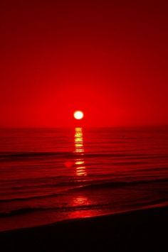 the sun is setting over the ocean on a red and black day with no clouds