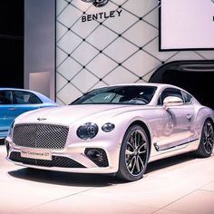 two bentley cars are on display at an auto show, one is white and the other is blue