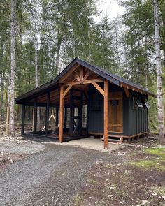 a small building in the middle of a forest with trees around it and gravel road leading up to it