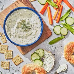 a table topped with bagels and cucumbers next to crackers covered in ranch dressing