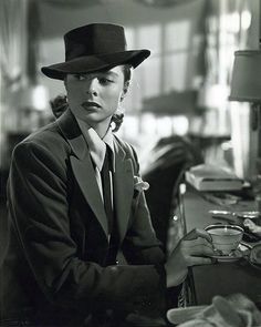 black and white photograph of a woman wearing a top hat sitting at a table with coffee