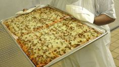 a man holding a tray with a large pizza on it's bottom and sides