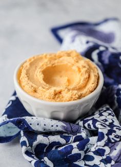 a white bowl filled with hummus sitting on top of a blue and white cloth