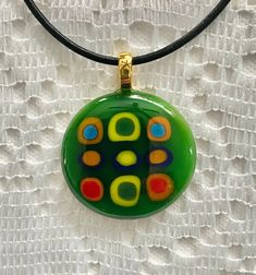 A unique, kiln fused glass pendant, custom designed for you, with floating vibrant, multi-colored blocks stacked in a variety of colorful rows encircled by the dark green edges upon a light green base.  A 16 inch black leather cord necklace with a 1.5 inch chain extension & nickel-free, silver-plated chain & clasp is included.  A fashionable & stylish, chic & modern mosaic glass necklace.  Dress up blue jeans, relax in loungewear or accent evening attire.  Created & handcrafted in a home worksho Artistic Green Glass Jewelry, Handmade Modern Green Jewelry, Green Handmade Modern Jewelry, Modern Handmade Green Jewelry, Modern Green Handmade Jewelry, Green Glass Pendant Jewelry, Modern Green Necklace As A Gift, Modern Green Necklace As Gift, Modern Green Necklace For Gift