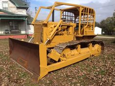 an old yellow bulldozer sitting in the middle of a yard with leaves on the ground