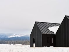 two black buildings sitting in the snow with mountains in the backgrouds behind them