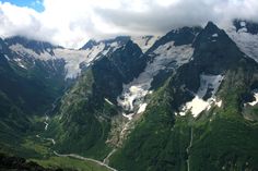 the mountains are covered in snow and green grass, with a river running between them