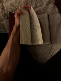 a person is reading a book on the bed while holding it in their hand with both hands