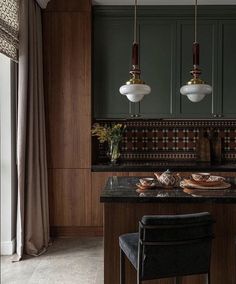 a kitchen with green cabinets and marble counter tops, two hanging lights above the island