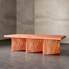 an orange marbled bench in front of a gray wall and concrete flooring area