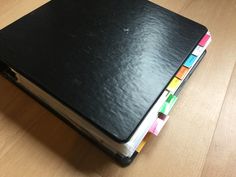 a black notebook with colored sticky notes attached to the cover on a wooden table top