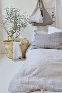 a bed with white linens and pillows next to a potted plant