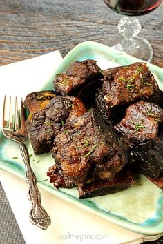 a green plate topped with meat next to a glass of wine