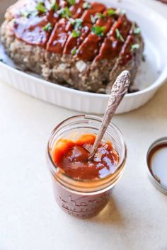 a jar filled with sauce sitting next to a plate of meatloaf on a table