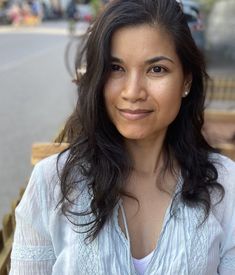 a woman with long dark hair is sitting on a bench and smiling at the camera