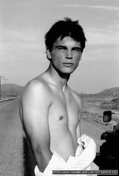 a man with no shirt standing next to a motorcycle on the side of the road