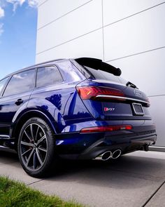 the rear end of an audi suv parked in front of a building with grass and blue sky