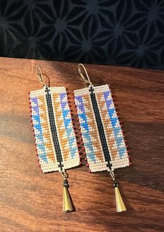 pair of beaded earrings with tassels on wooden table next to black wall